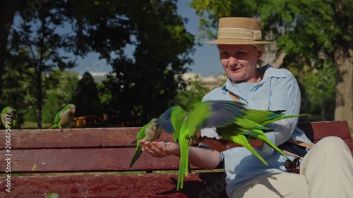 Woman feeding monk parakeets on park bench in Ciutadella Park near Arc de Triomf in Barcelona