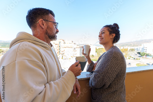 Couple enjoying morning coffee and intimate conversation on sunny apartment balcony overlooking the city