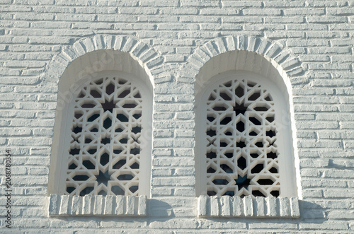 White brick wall with traditional Arabic geometric lattice windows. Moorish architecture facade in Spain