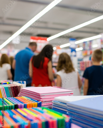 People choosing colored notebooks, pens, and school supplies in a supermarket aisle, preparing for the upcoming academic year and blurred background