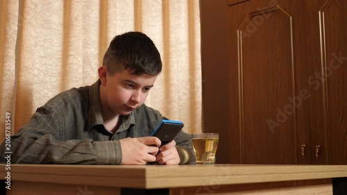 Teenager focused on playing a handheld gaming console while sitting at a table at home, with a cup of tea nearby.