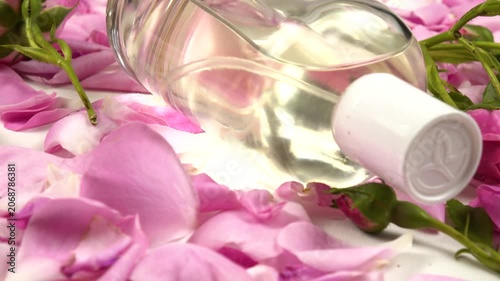 Bottles with perfumes and eau de toilette with use rose essential oil, fresh pink roses are on a white table, side view