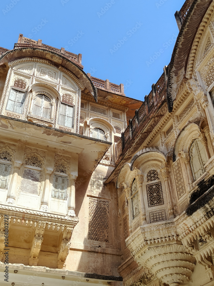Obraz premium Ornate sandstone palace facades and jharokha balconies seen from below at Mehrangarh Fort in Jodhpur, India.