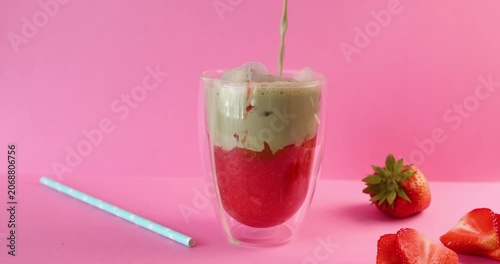 Pouring organic strawberry smoothie into empty glass for commercial food marketing. Healthy premium beverage option highlights vibrant red berry colors on uniform studio background. Professional