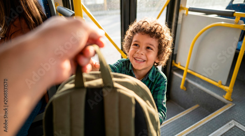 Happy young boy with curly hair receiving a backpack on a public transport bus