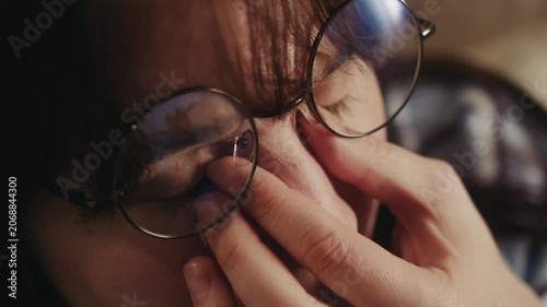 Close-up portrait of tired woman adjusting eyeglasses and rubbing eyes. Female experiencing eye strain, fatigue, stress or headache while working indoors. Vision problems, exhaustion and health