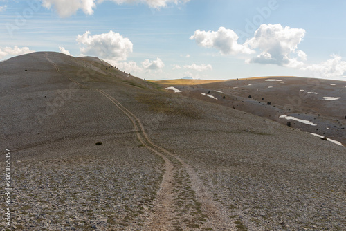 A mountain trail in a treeless mountain range with clouds in a blue sky