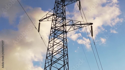 Large steel power line tower carrying multiple electricity transmission wires across the expansive blue sky filled with scattered white and golden clouds during daytime