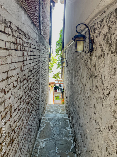 Vertical eye level shot of an extremely narrow cobblestone passage between rustic brick and stucco walls with a vintage wrought iron lantern in the historic old town of Nesebar, Bulgaria