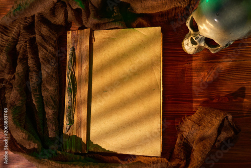 Ancient volume with skull lighting. Eerie still life composition featuring vintage book and skull under green illumination
