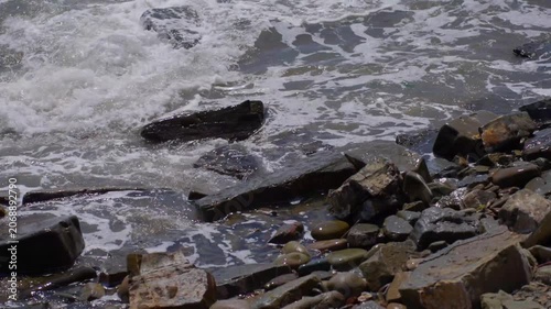 Rocky shoreline sequence with waves progressively covering stones late in clip