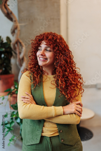 Young redhead woman smiling with crossed arms in office