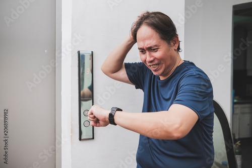 Fotografie Southeast Asian man reacts with frustration after waiting too long for an elevator, causing him to be late
