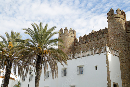 The historic Palace of the Dukes of Feria with its distinctive stone towers and battlements behind a white facade and palm trees in Zafra, Badajoz, Spain