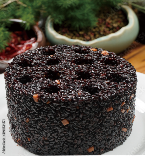 Black rice balls shaped like honeycomb briquettes are served on a white round porcelain plate.