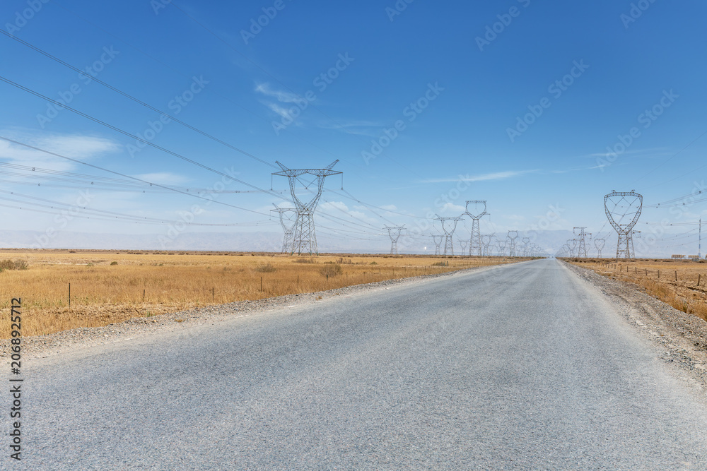 Fototapeta premium Desert Highway Stretching Toward Distant Transmission Towers Under Clear Blue Sky