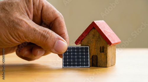 Hand solar panel toy house renewable energy wood model placing home adult hand placing solar panel beside wood toy house for clean power concept