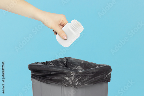 throwing plastic jar with vitamins into trash, outstretched hand with plastic jar with vitamins in front of trash can