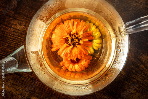 Fresh calendula herbal tea in a glass teapot, a flat lay