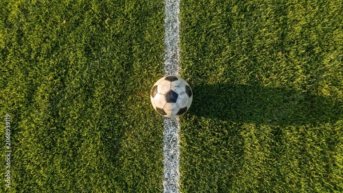 Soccer ball on the white touchline of a green football field at stadium under bright sunlight, perfect for sports training, match competition, or athletic championship concept