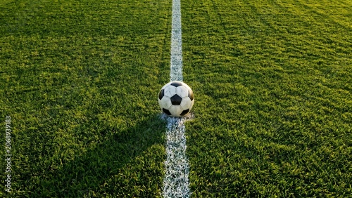 Soccer ball on the white touchline of a green football field at stadium under bright sunlight, perfect for sports training, match competition, or athletic championship concept