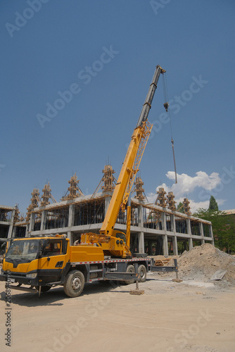 Active construction site featuring a yellow mobile crane and a multi-story concrete building frame under a clear blue sky.