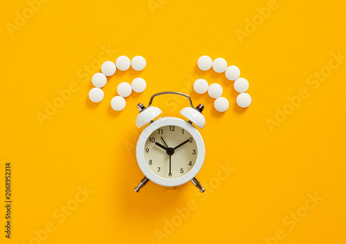 White alarm clock and pills forming question marks on yellow background