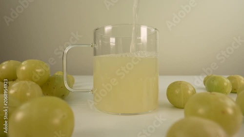 Fresh Indian gooseberry juice pouring into a glass cup. Amla juice. Phyllanthus emblica.