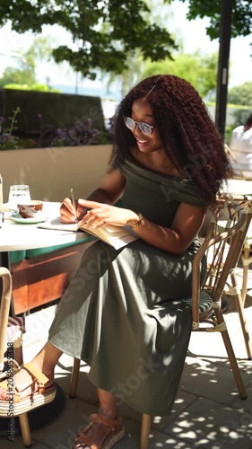 Young woman in a cafe outdoors writing in a notebook on a sunny day