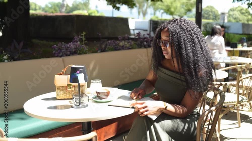 Young woman in a cafe outdoors writing in a notebook on a sunny day