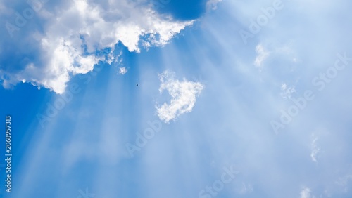 Fotografi Sunlight breaking through clouds in a bright blue sky.