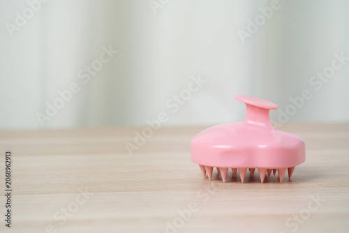 Soft pink silicone scalp massager brush with conical nubs on a wooden surface, shampoo massages, scalp exfoliation and improved circulation for gentle at-home hair care and bathing routines.