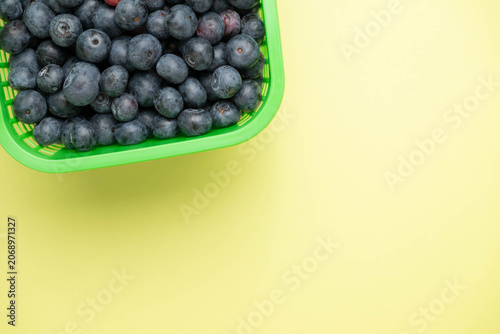 Fresh picked blueberries in a bright green basket on a light green background.