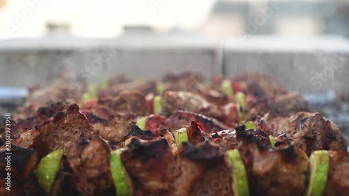 Pork meat skewers with zucchini and tomato slices cooking on charcoal grill with rising smoke. Close up barbecue footage with shallow depth of field. Outdoor summer cooking and picnic concept. 