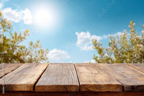 Empty wooden table top with green treetops and bright sunlight background