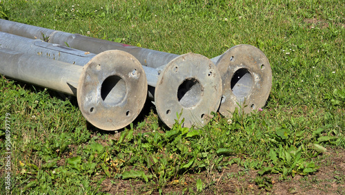 Fotografie Galvanized steel utility poles with circular mounting flanges on green grass