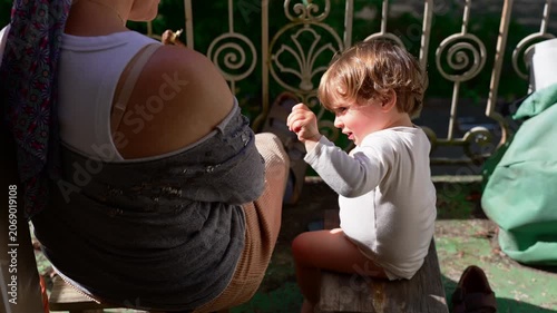 Mother and toddler sitting together on sunlit balcony, peaceful family moment as young child reaches for attention, expressing attachment, trust and emotional connection