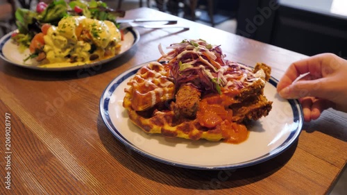 Close view of chicken and waffles on plate, woman turns it to show dish from all angles. Classic brunch or late breakfast meal, served at trendy cafe in Hong Kong, highlighting modern food culture