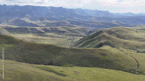 Wide Aerial Of Rolling Green Hills And Distant Drakensberg Peaks, Hiking Guide Leads Visual Journey