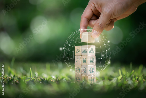 Hand Stacking Wooden Cubes with IT Network Icons and Virtual Global Connection Sphere Graphic on Green Grass for Eco-Friendly Digital Infrastructure and Green Tech Concept