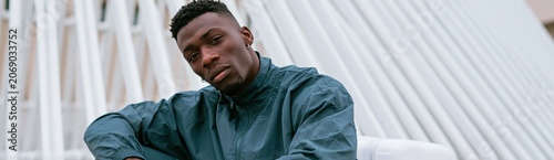 Close up portrait of a young man in a blue tracksuit leaning by a white railing for urban fashion banner and background design