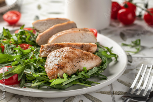 Grilled chicken breast and green vegetable salad on white plate close up, healthy food and diet concept on printed tile background