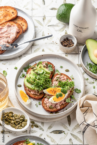 Healthy avocado and egg toasts sprinkled with microgreens and pumpkin seeds on printed tile background