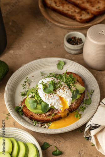 Healthy avocado and poached egg toast sprinkled with microgreens on beige textured background. Healthy morning breakfast