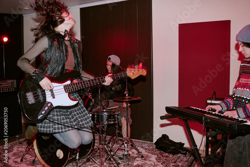 Teenage girls performing in music group, playing bass guitar, drums, keyboard during rehearsal or live session. Useful for youth band promotion, music education, entertainment marketing