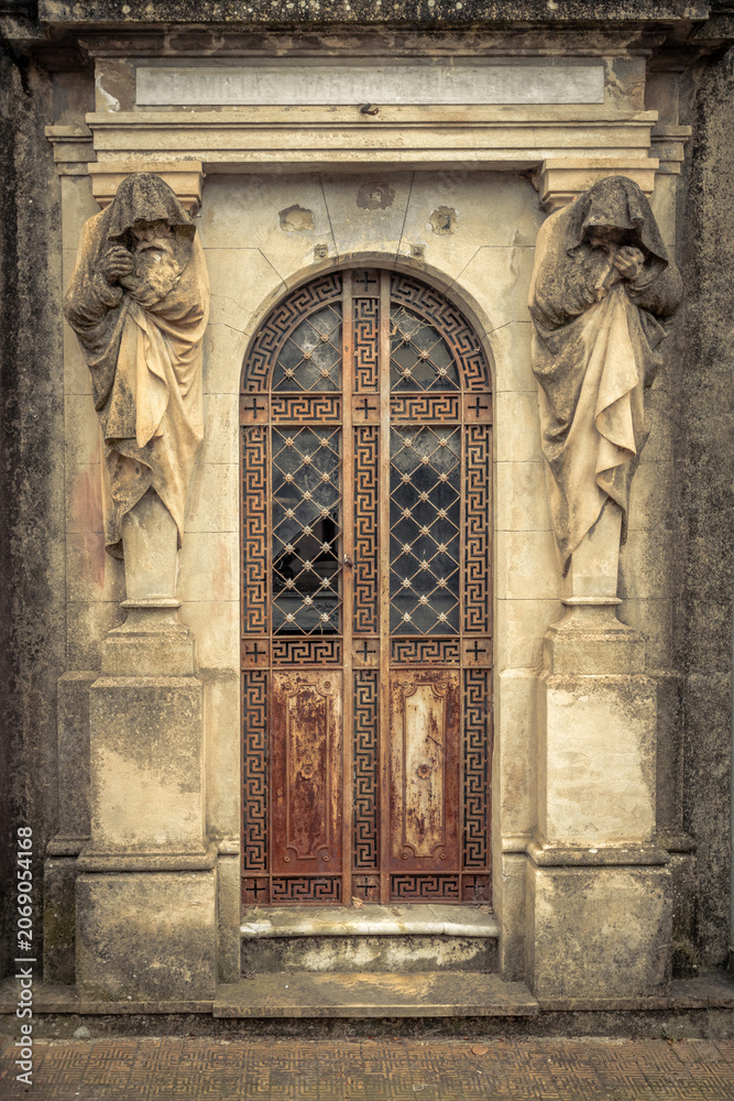 Fototapeta premium Weathered Mausoleum Entrance with Mourning Statues and Ornate Door