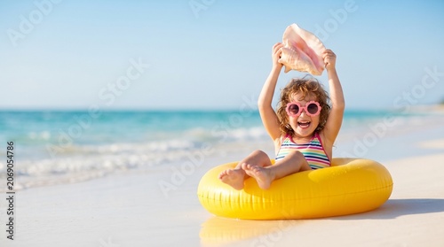 Happy toddler girl with seashell and yellow float on tropical beach