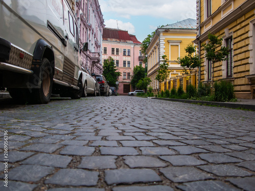 Exploring a quiet stone street in Chernivtsi, Ukraine, with parked cars on both sides and buildings in the background
