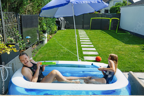 Escaping the heat and cooling off at home – a happy family splashing each other in a small garden pool.