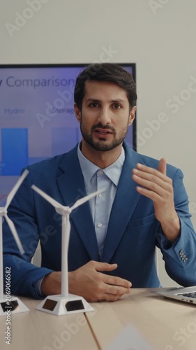 Portrait of Hispanic man engineer presents renewable power generation in office vertical shot. Latin American expert explains project with windmills models
